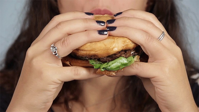 Người ăn cầm hai tay chiếc burger dày kiểu Mỹ